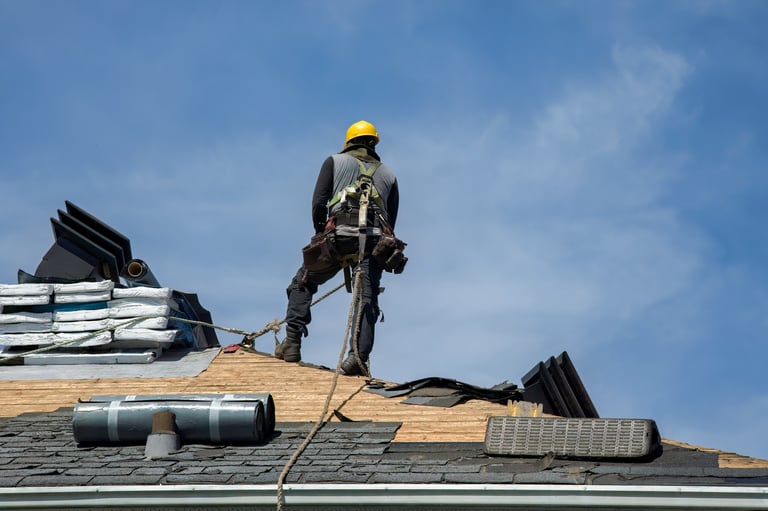 Construction worker applying roofing materials with safety helmet against blue sky