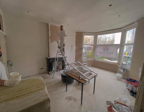 Interior room under renovation with exposed walls, work table, ladder, and large curved window overlooking street