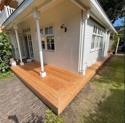White cottage with wooden deck and covered porch supported by white columns