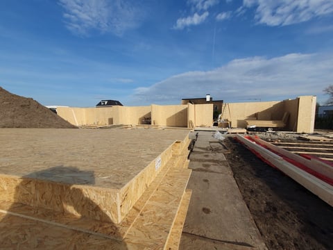 Construction site with large beige concrete structures, equipment, and bare earth under blue sky
