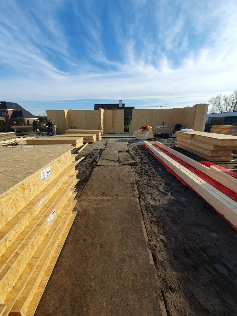 Construction site with wooden wall frames, insulation materials, and building materials on dirt foundation under blue sky