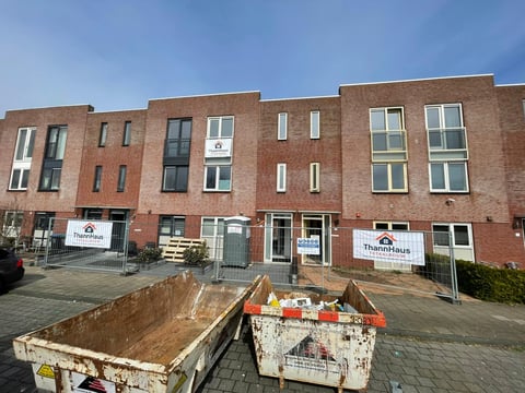 Row of brick residential buildings with ground floor shops, parked dumpsters, and clear blue sky