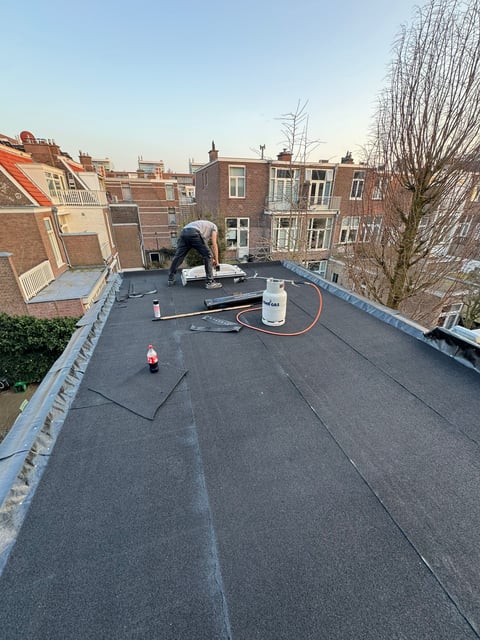 Worker applying roofing material on a flat residential roof in an urban neighborhood