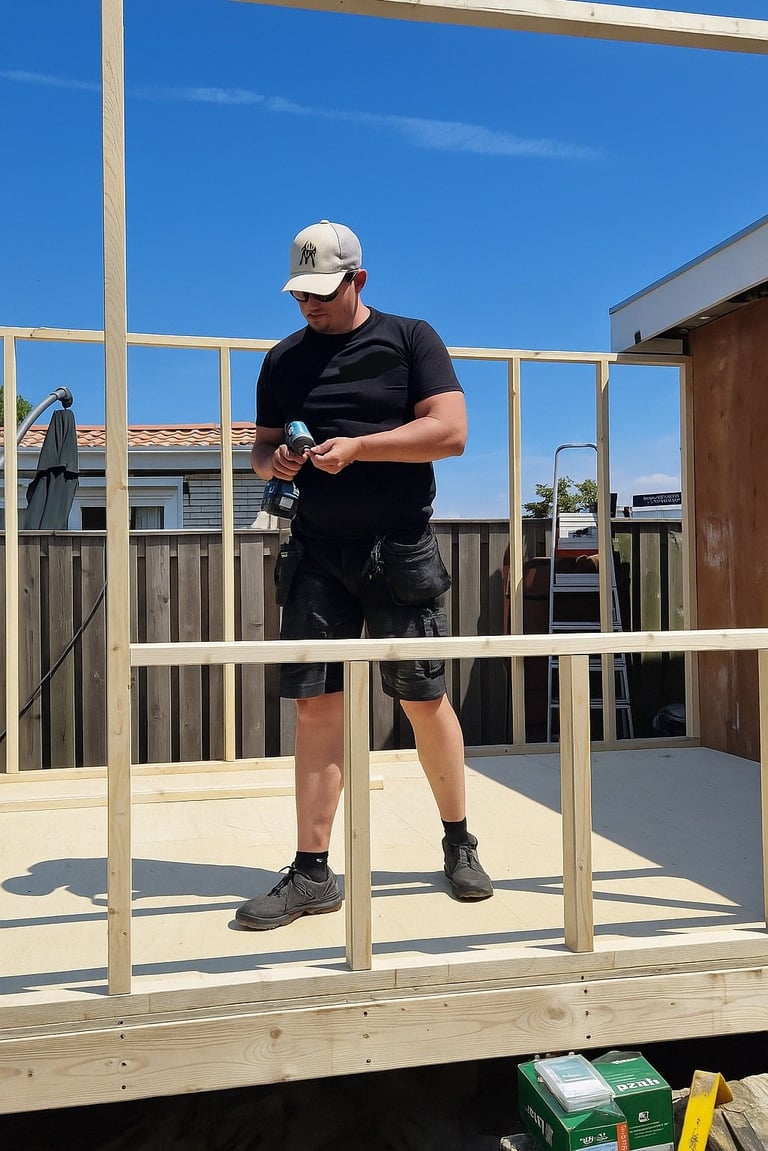 Man in black shirt and cap working on wooden deck framing under clear blue sky