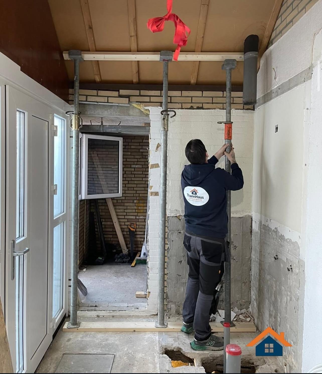 Worker in dark jacket installing metal support frame in unfinished interior construction area with exposed brick and white walls